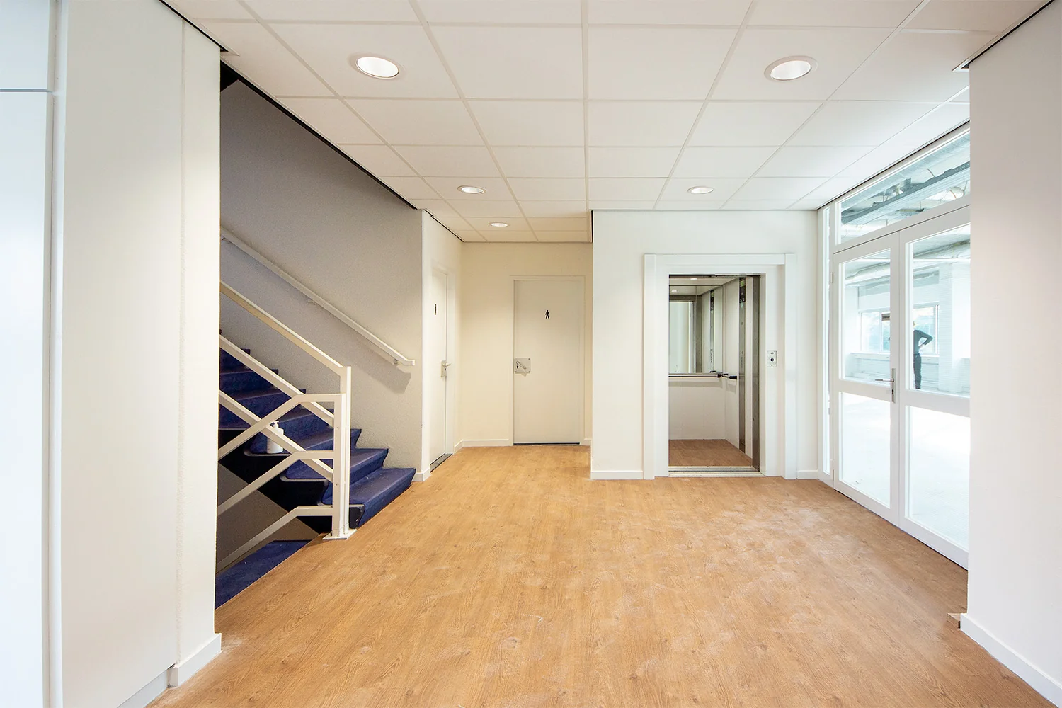 Hal van een bedrijfsgebouw aan de Huis-ter-Heideweg met een trap, lift en houten vloer.